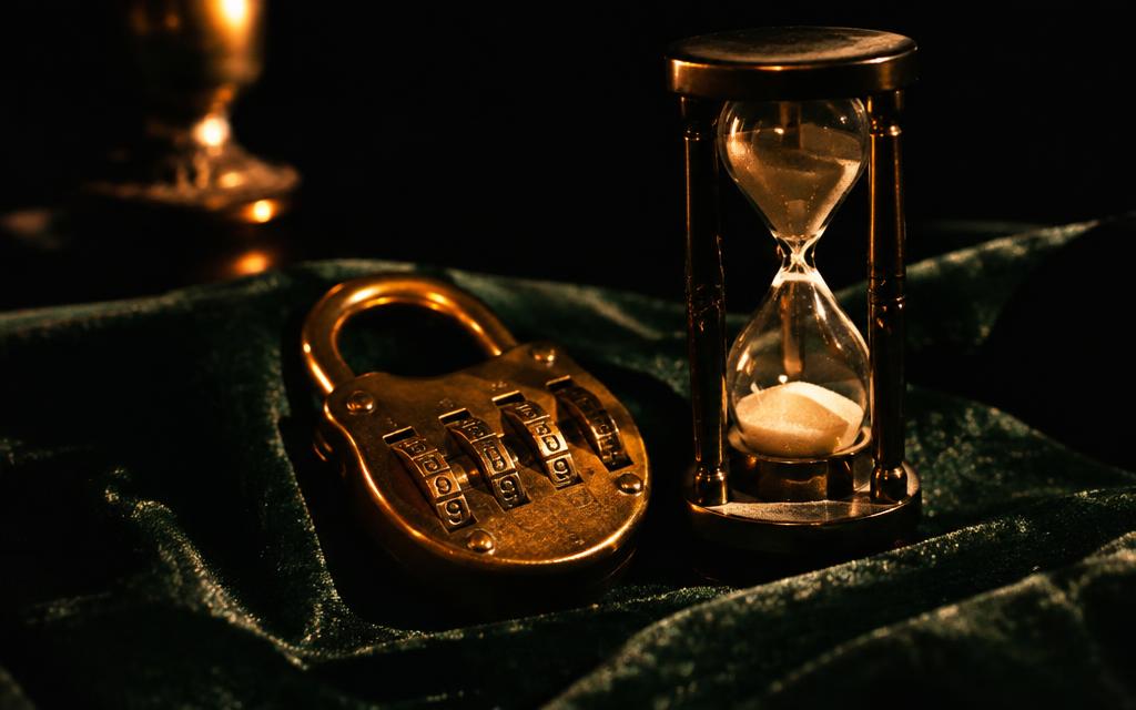 Candado de bronce y reloj de arena sobre terciopelo verde